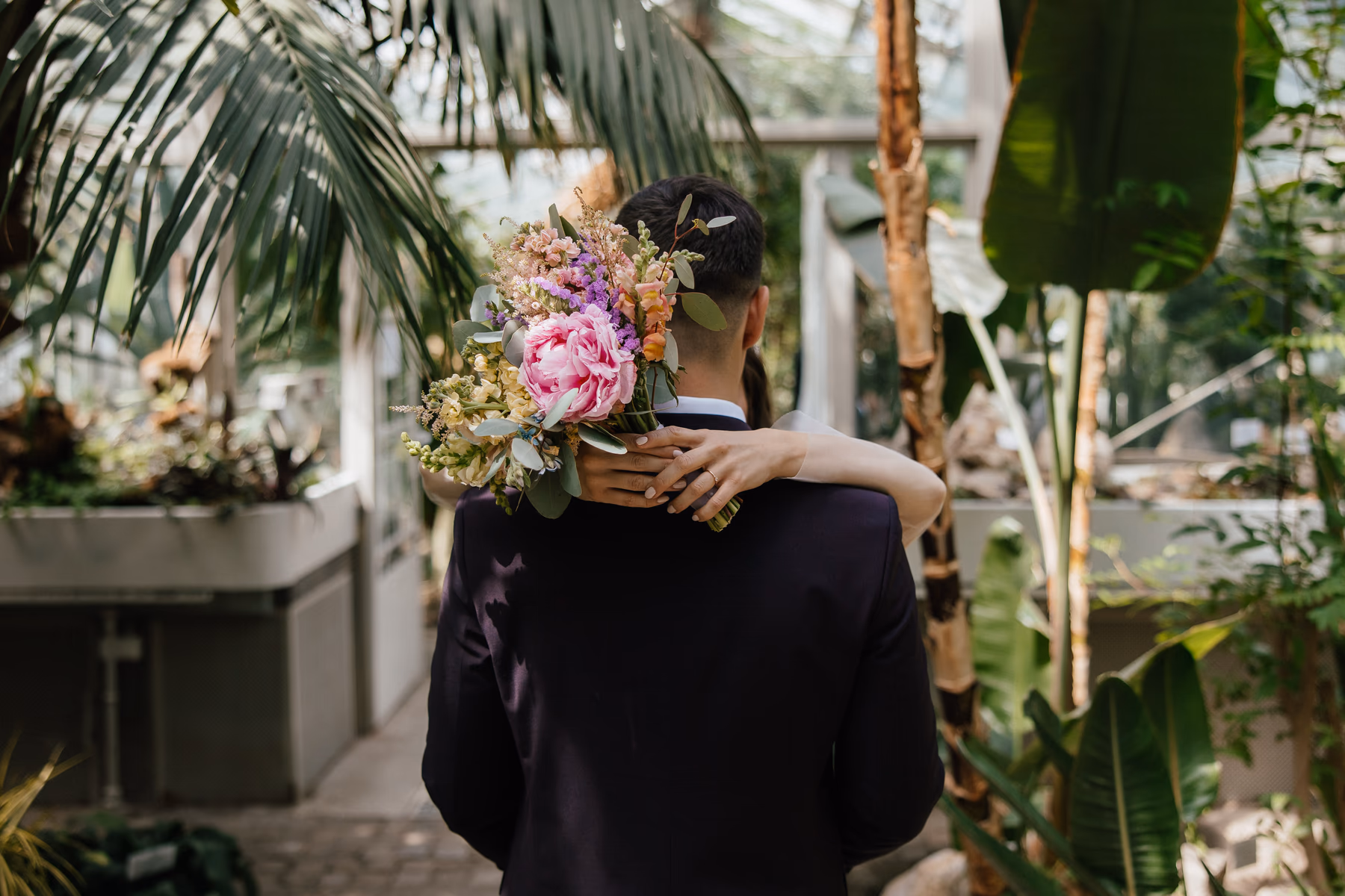 Newlyweds embracing in a greenhouse, with the bride holding a bouquet